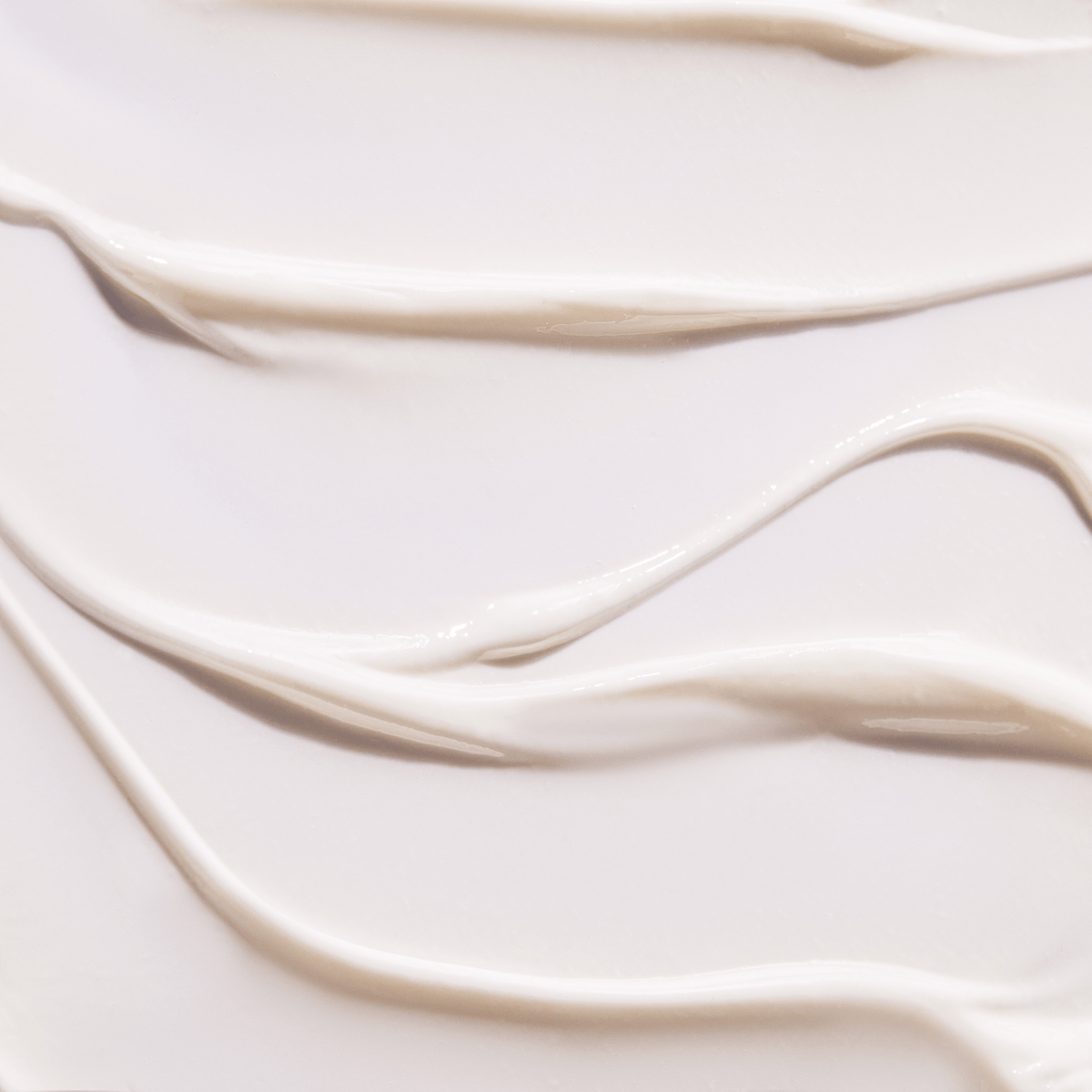 Close-up texture of smooth, creamy lotion or moisturizer spread in soft, wavy lines on a light surface.
