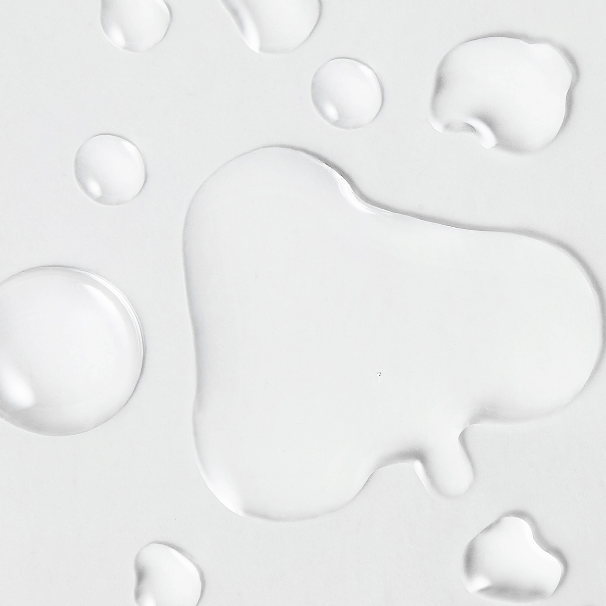 Close-up texture of the goPure Refine It! 2% BHA Liquid Exfoliant, showing clear liquid droplets spread across a smooth white surface. The image highlights the lightweight, watery consistency of the exfoliant formula.